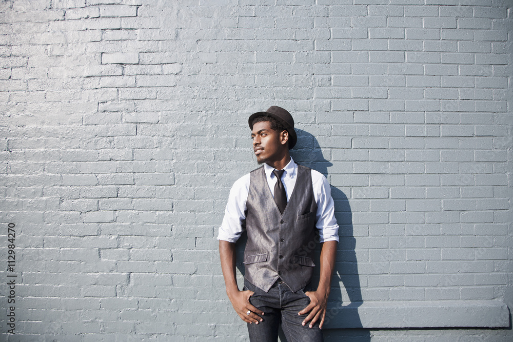 A young black man leaning against a brick wall